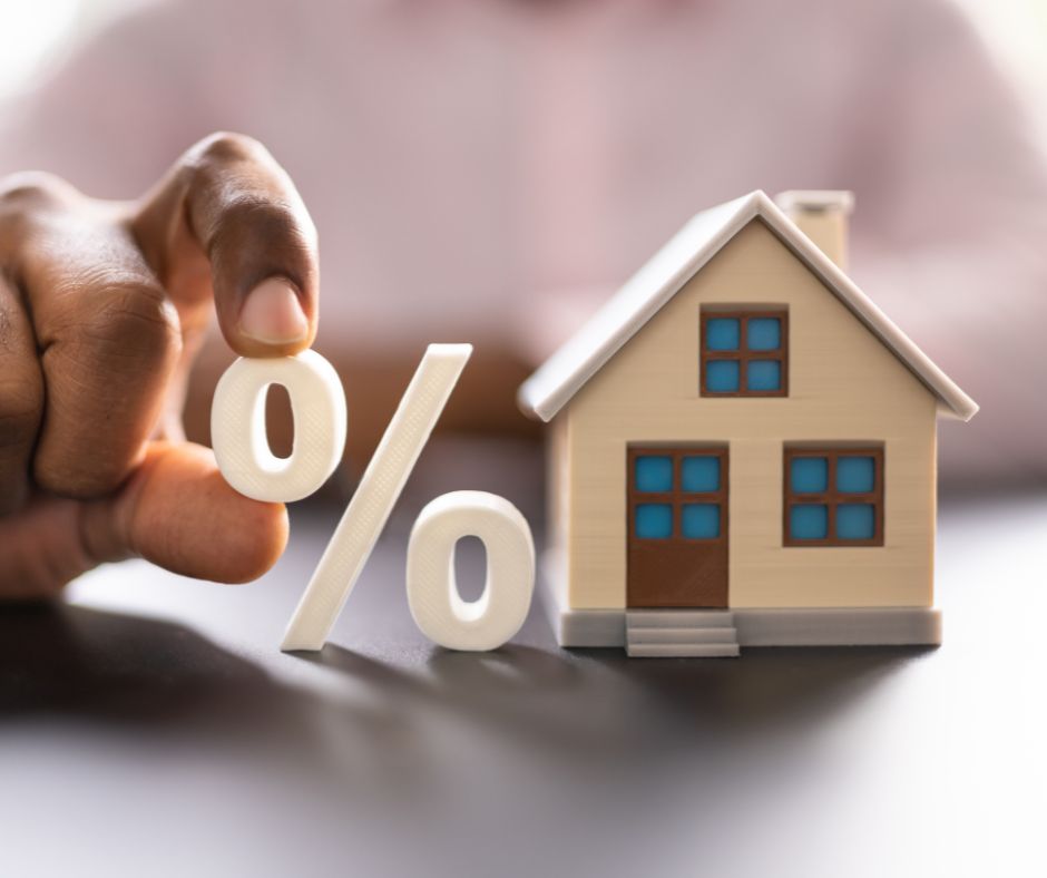 A hand holding a percentage sign next to a toy house