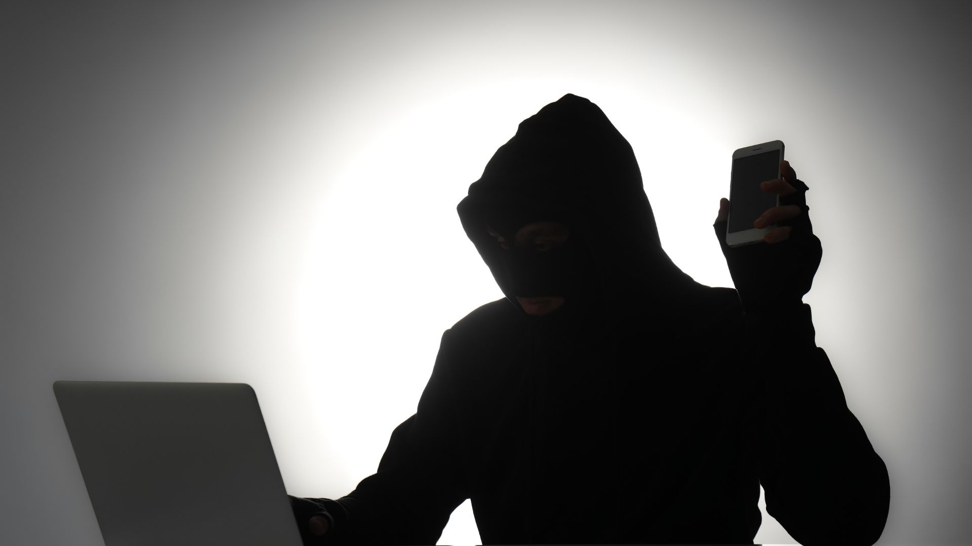 A scammer holding a phone and a laptop